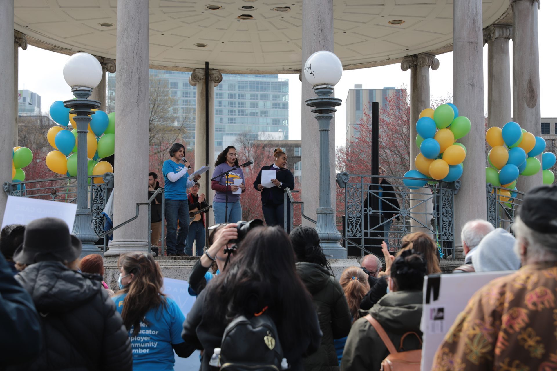 A crowd of people are gathered under a gazebo with balloons.