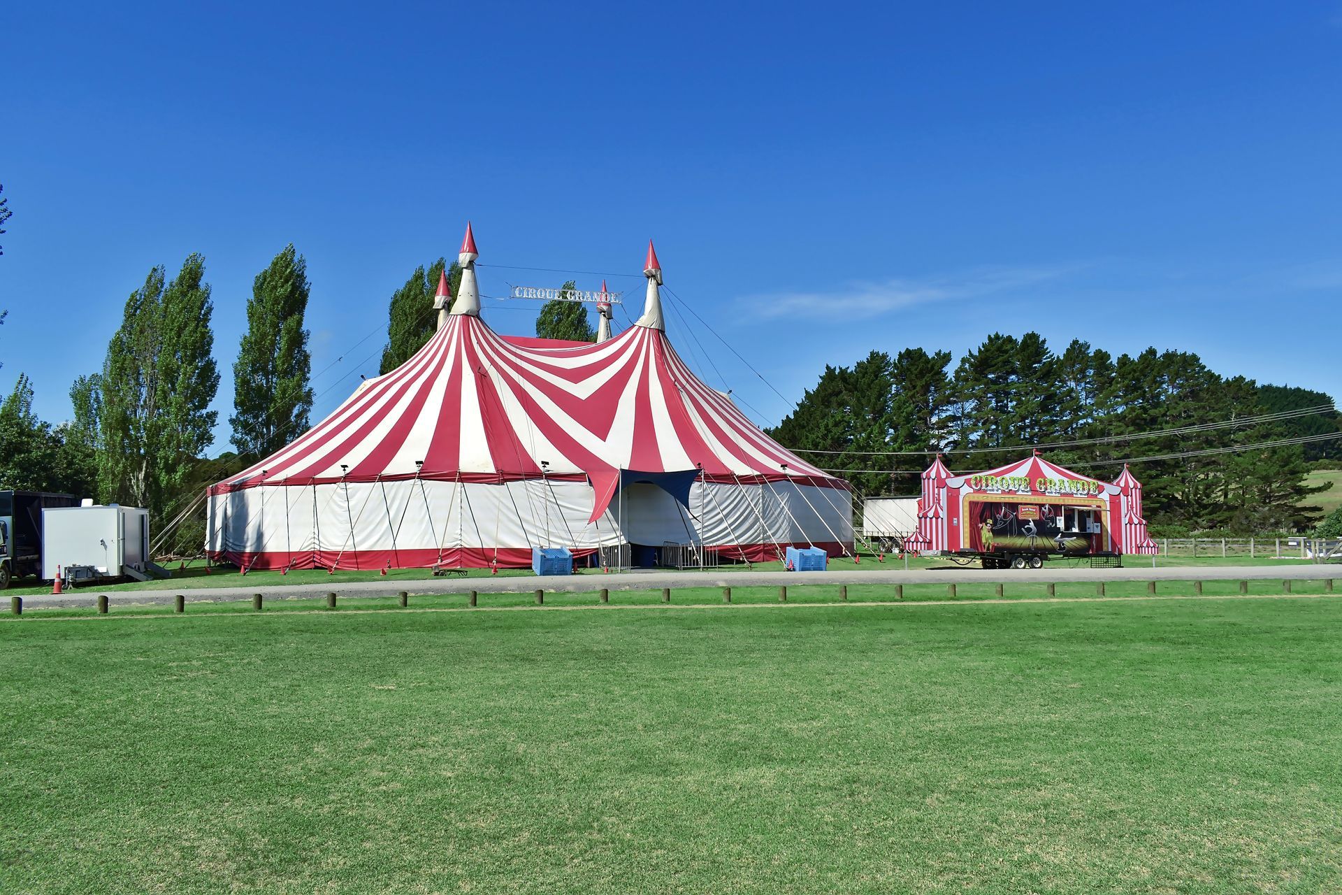 A red and white circus tent is sitting in the middle of a grassy field.