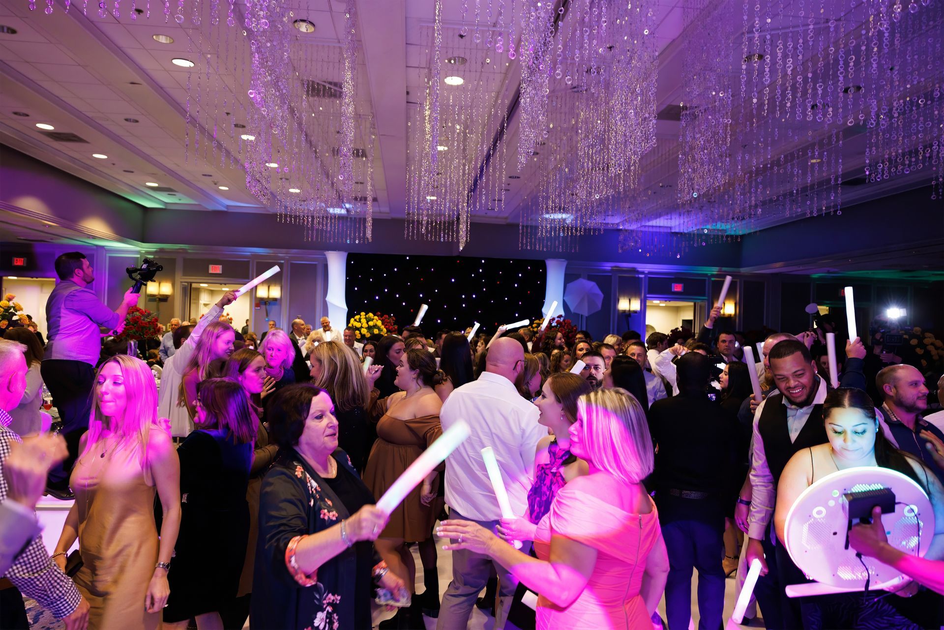A large group of people are dancing in a large room at a party.