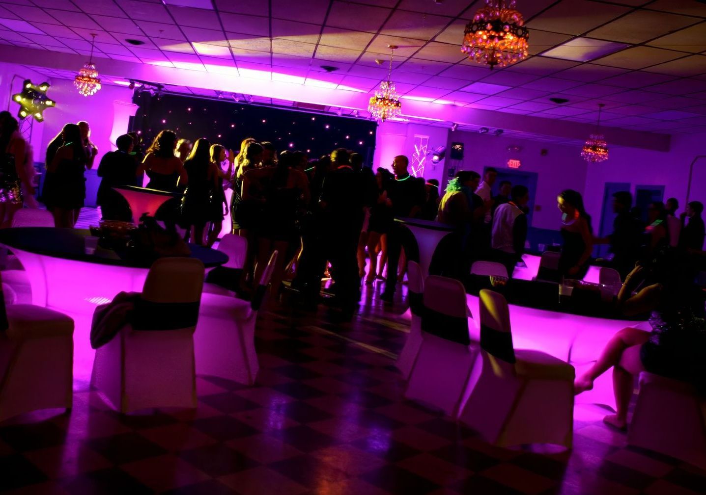 A crowd of people are gathered in a room with purple lights