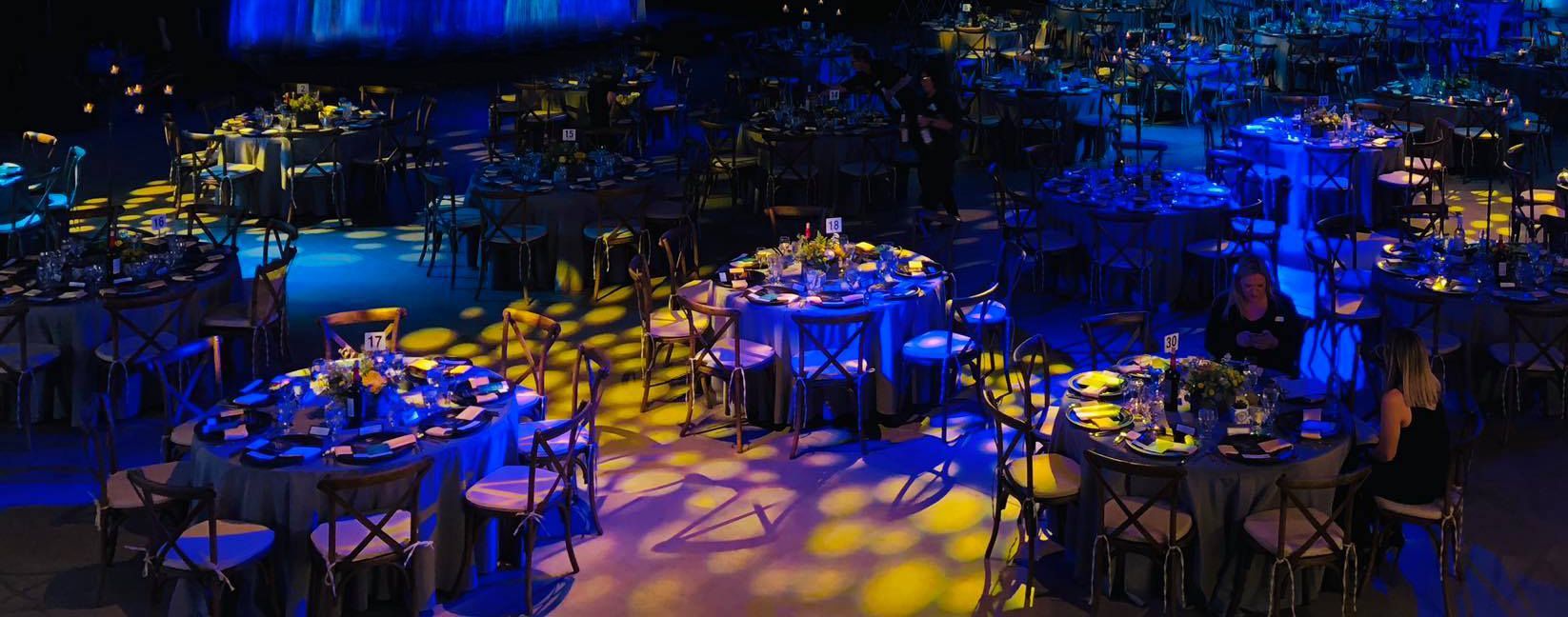 A large room filled with tables and chairs lit up with blue and yellow lights.
