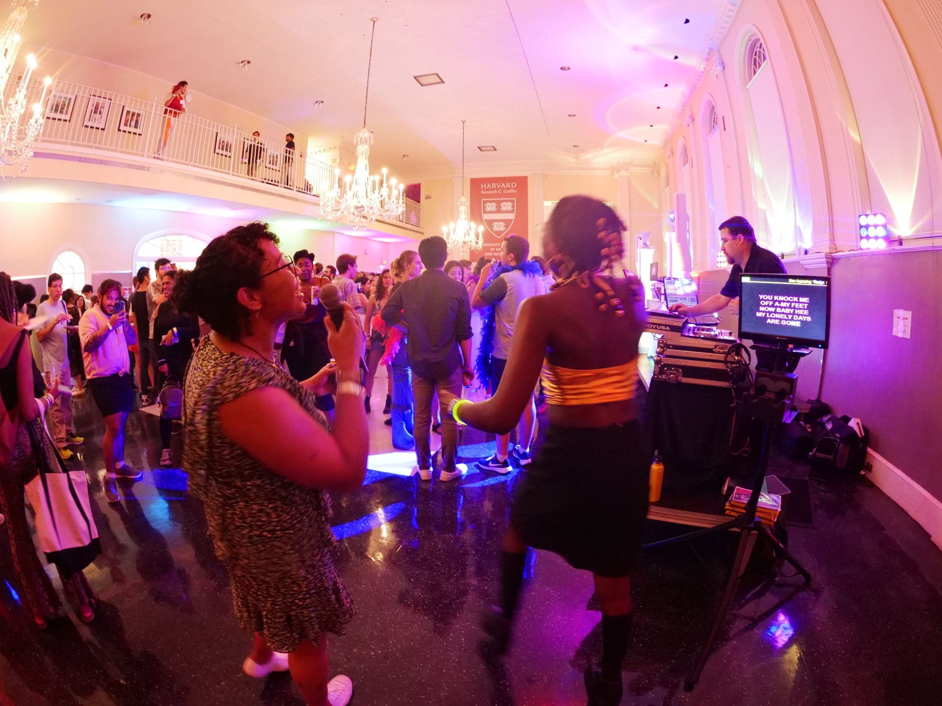 A group of people are dancing in a large room with purple lights.