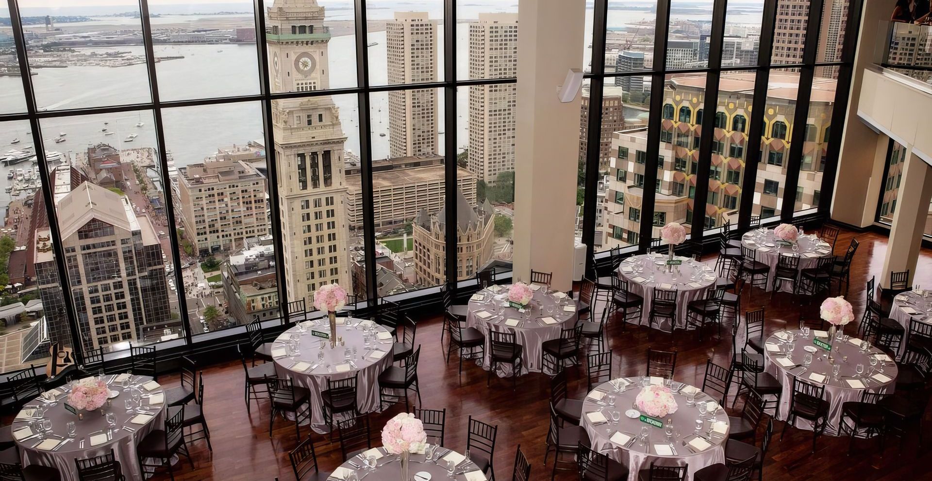 A large room with tables and chairs set up for a wedding reception with a view of the city.