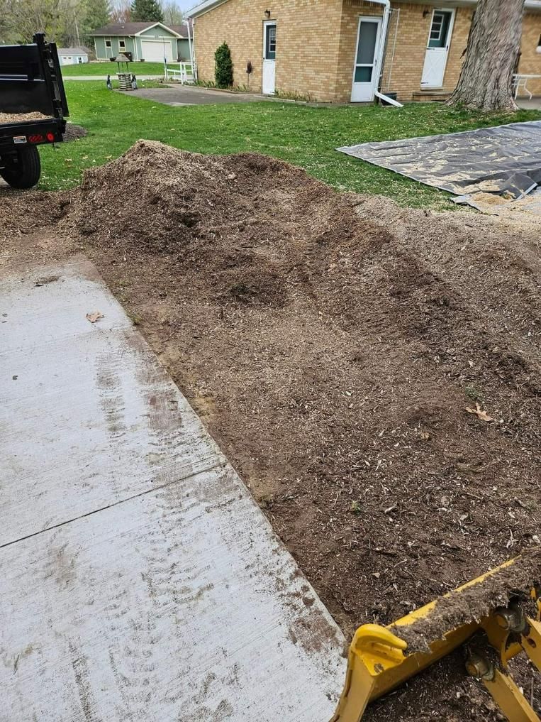 A large pile of wood chips next to a concrete driveway, likely for landscaping.