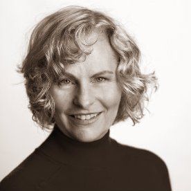 Woman with curly blonde hair smiles, wearing a black turtleneck.