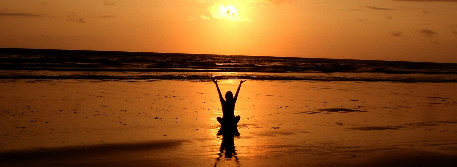 Silhouetted figures on a beach at sunset, one person on another's shoulders with arms raised.