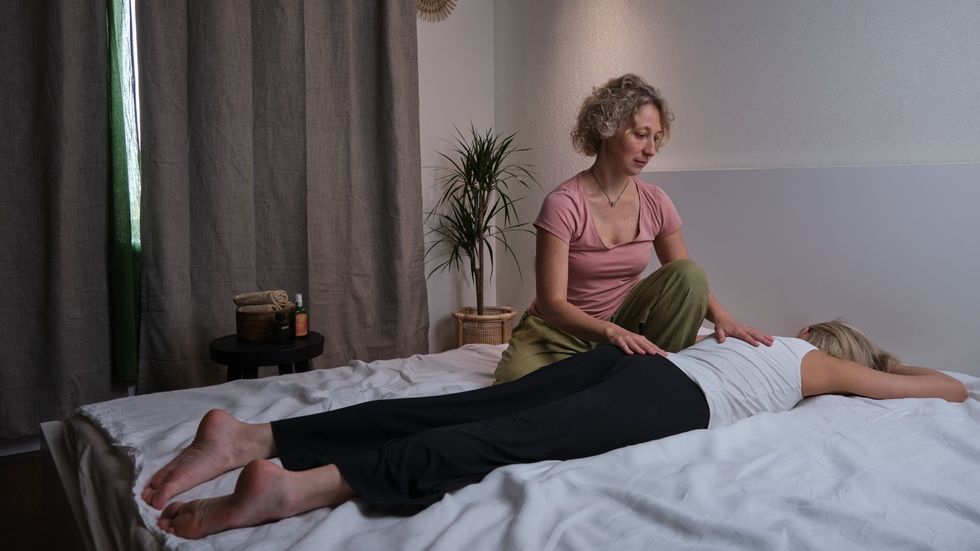 Person receiving leg massage on a massage table. Another person is manipulating their foot. Interior setting.