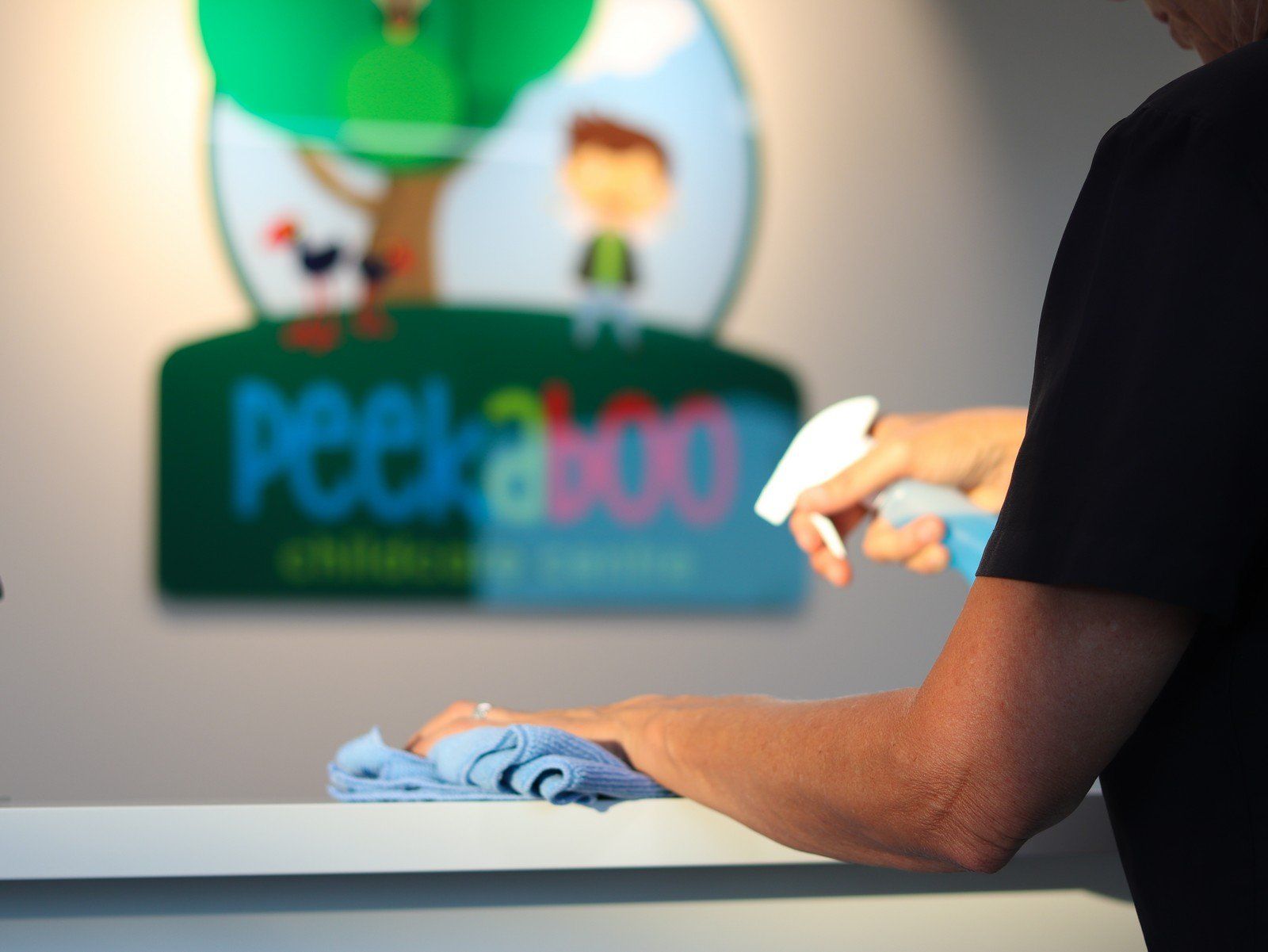 A person cleaning a counter in front of a peekaboo sign