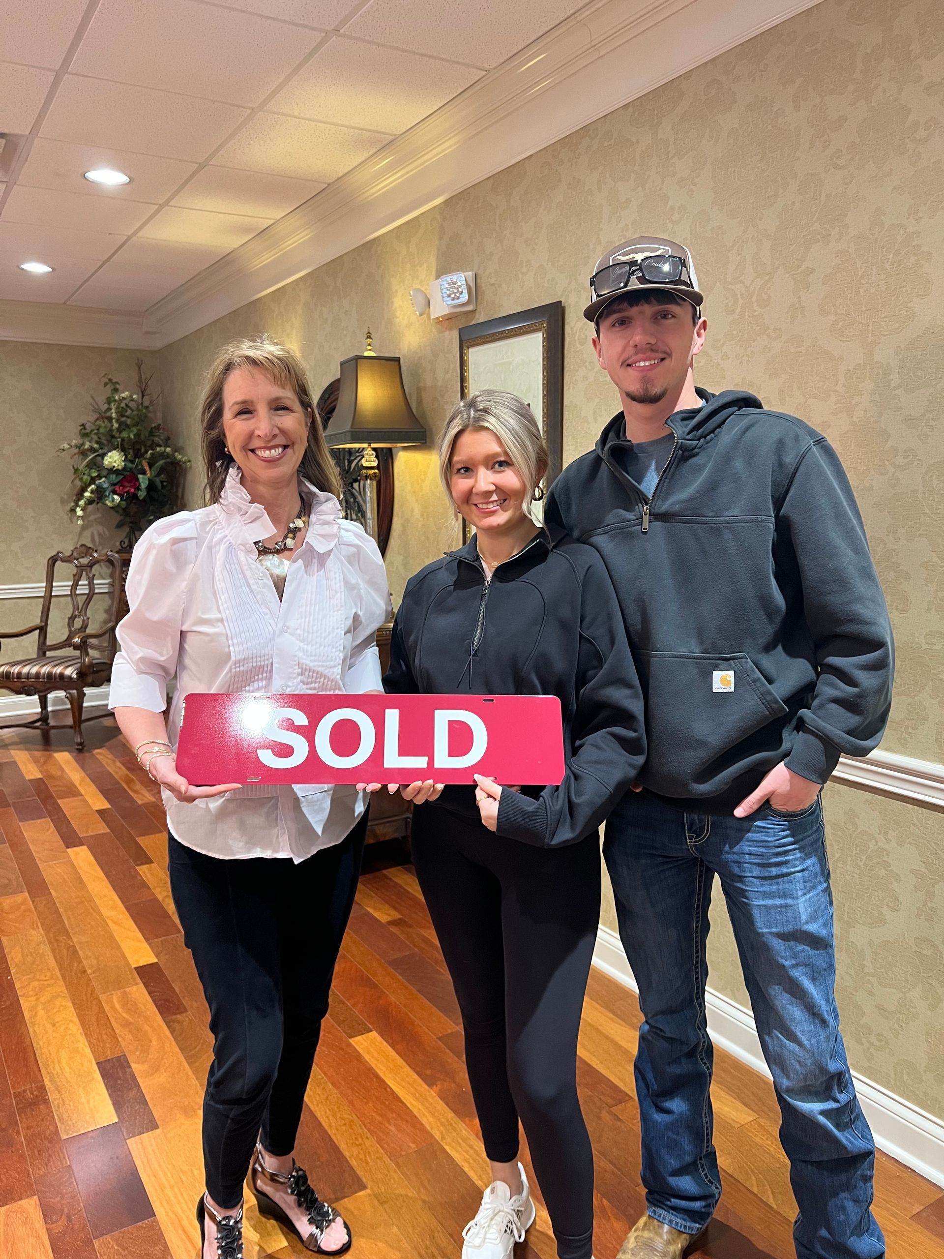 Three people stand indoors, smiling and holding a pink 