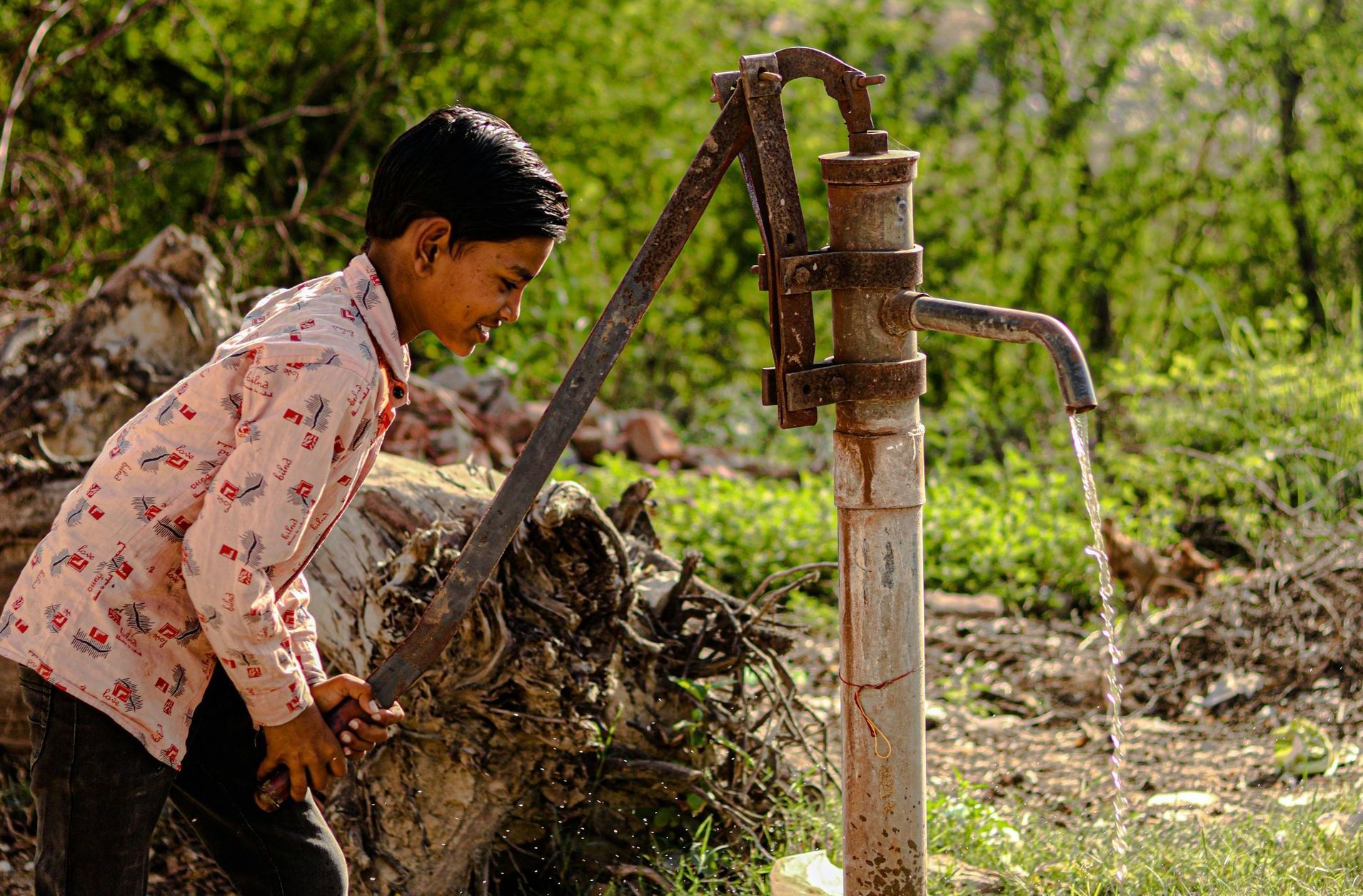 Un niño pequeño está bombeando agua de un pozo.