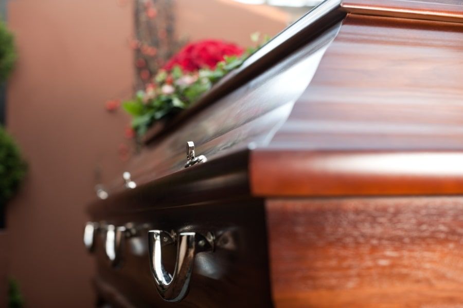 A polished wooden casket with metallic side handles, decorated with a floral arrangement of red roses.