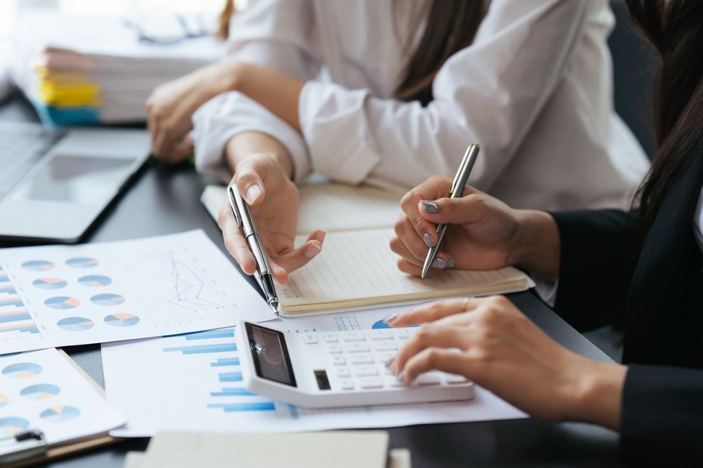 Two women working on financial documents with a calculator.