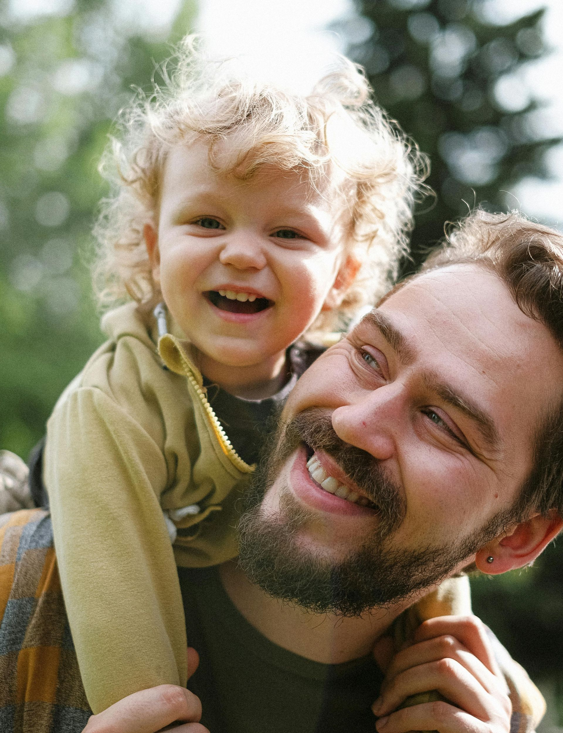 Father carrying a child on his shoulders; both smiling. Outdoors; natural light.