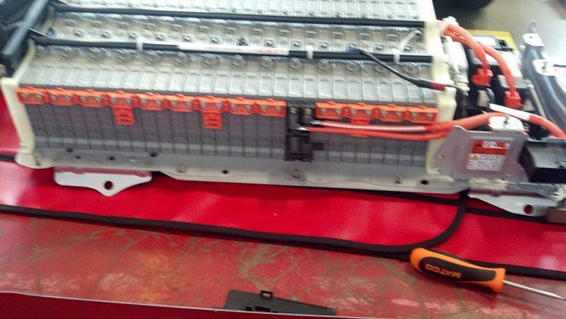 A battery is sitting on a red table next to a screwdriver | Autotrends