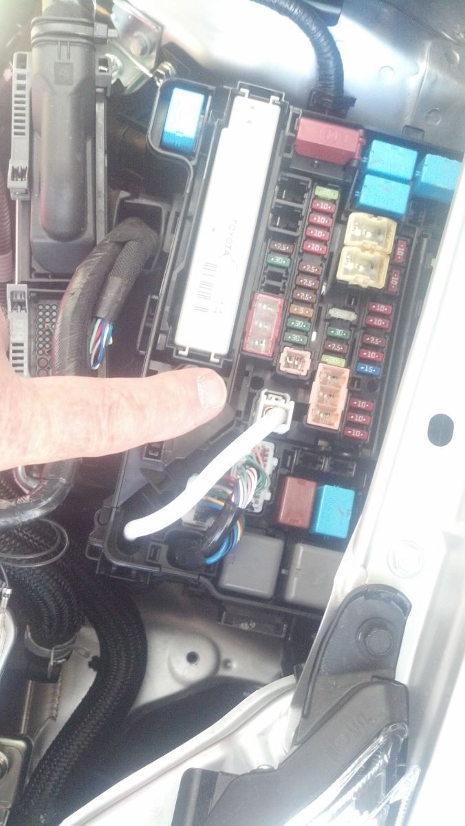 A person is pointing at a fuse box under the hood of a car | Autotrends