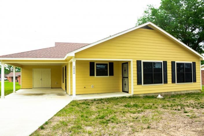 Yellow single-story house with black shutters, a carport, and a grassy front yard