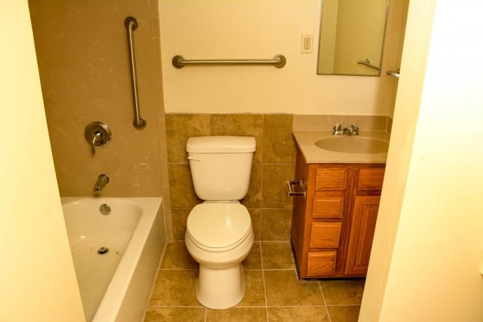 Bathroom with tub, toilet, and vanity in beige and wood tones