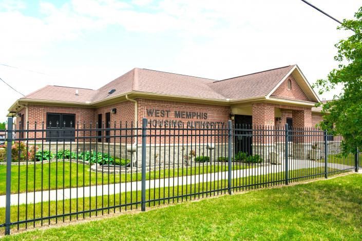 Brick church building behind a black metal fence with a green lawn and cloudy sky