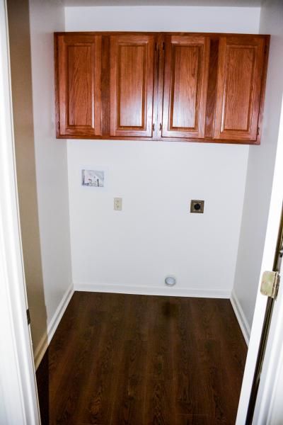 Small empty alcove with wooden wall cabinets, white walls, and dark wood flooring.