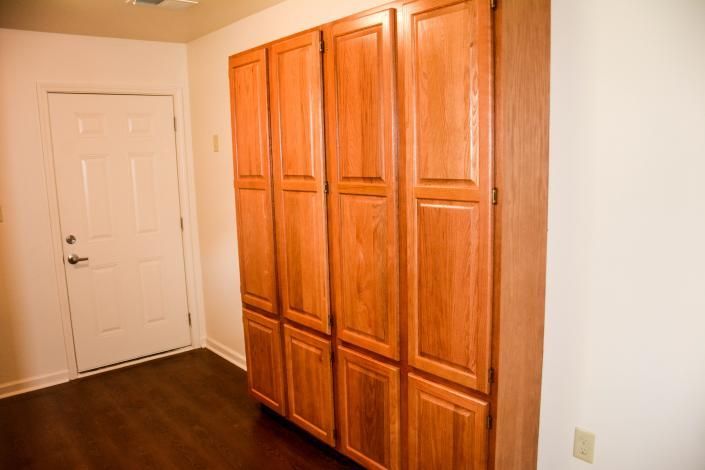 Empty room with a white door and wooden floor-to-ceiling cabinets along the wall