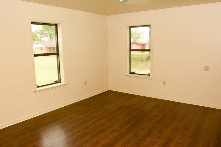 Empty beige room with wood floor and two small windows showing green lawn outside