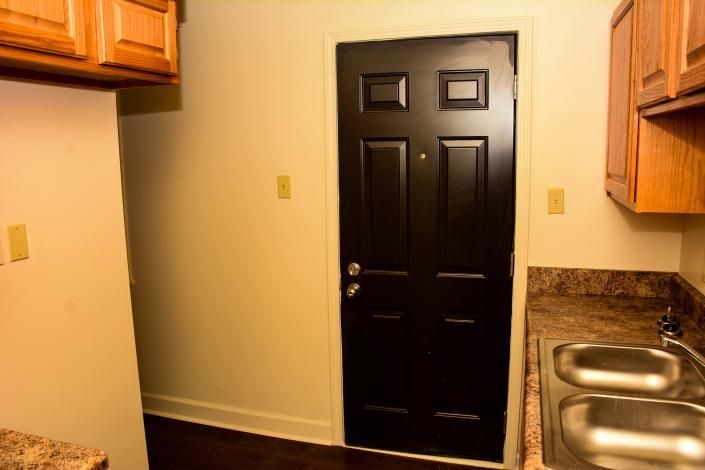 Small kitchen with black door, wood cabinets, and double stainless-steel sink.
