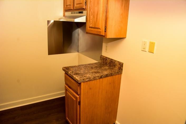 Small kitchen corner with wood cabinets, granite countertop, and a stainless steel range hood on a cream wall.