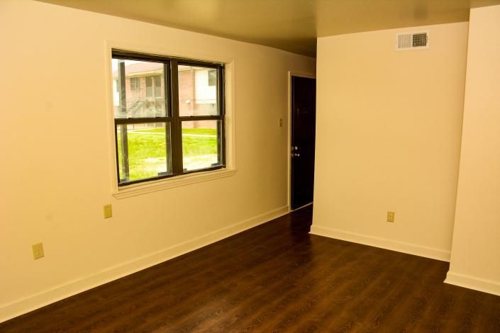 Empty room with beige walls, dark wood floor, and a window near a doorway.