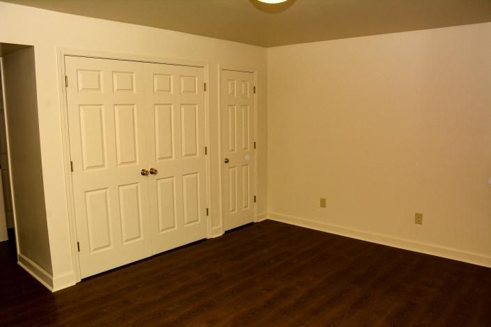 Empty beige room with dark wood floor, white double closet doors, and recessed ceiling light.