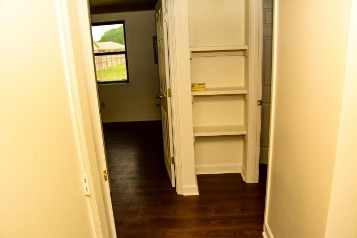 Empty hallway with dark wood floors, beige walls, and built-in shelves near a doorway.