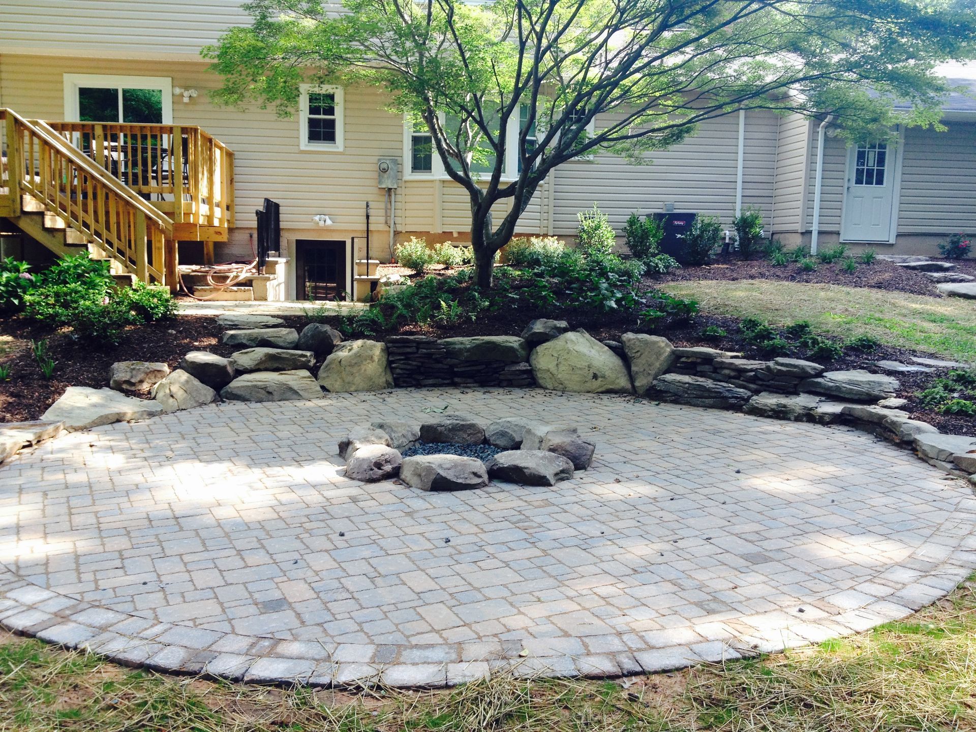 A fire pit is in the middle of a brick patio in front of a house.