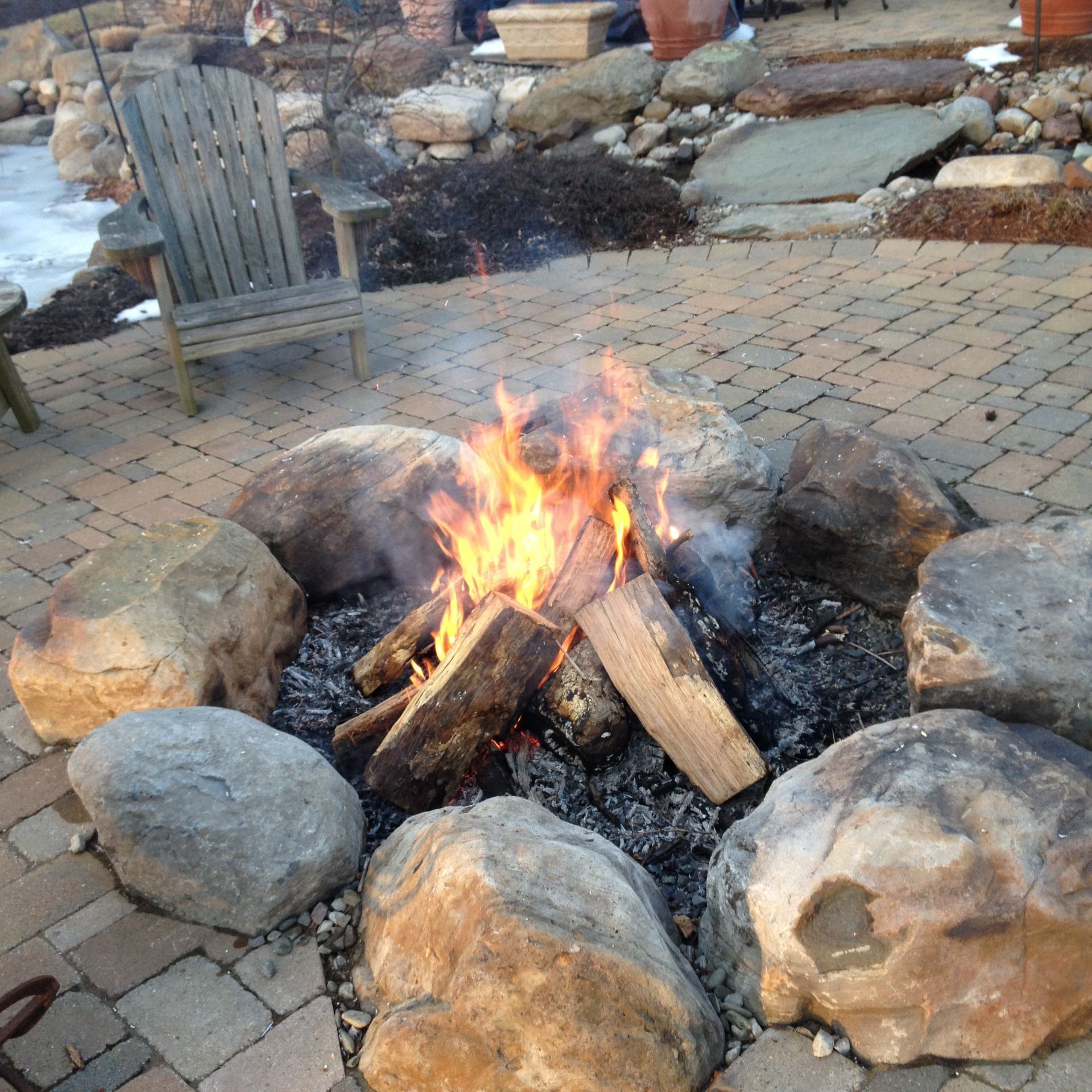 A fire pit surrounded by rocks with a chair in the background