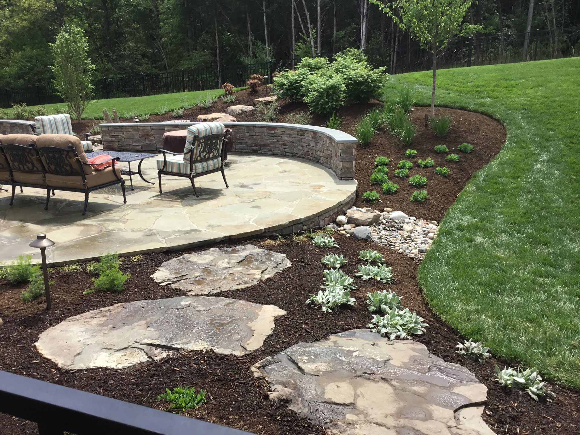 A patio with a couch and chairs in the middle of a lush green field.