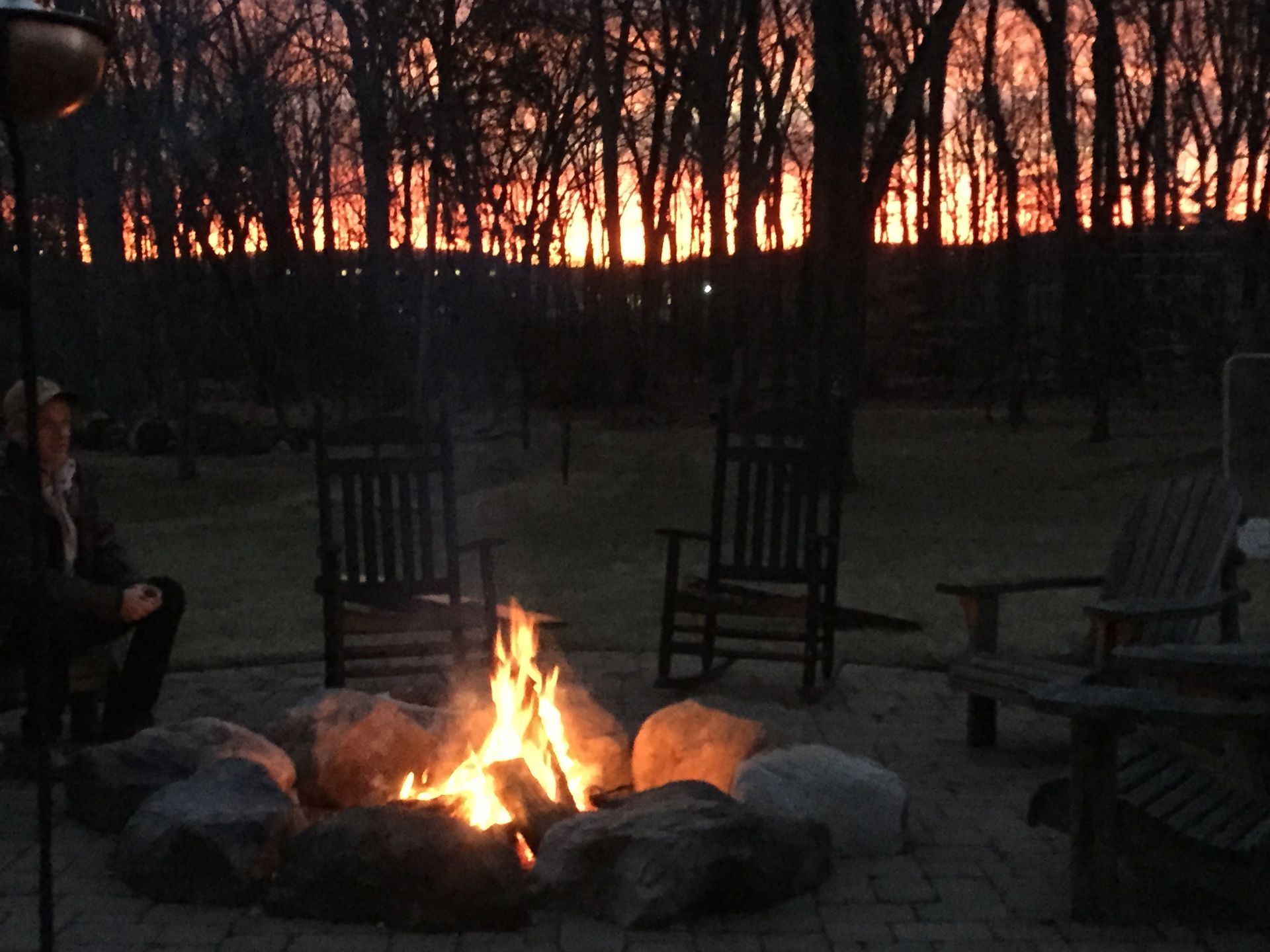 A fire pit with rocking chairs around it and a sunset in the background
