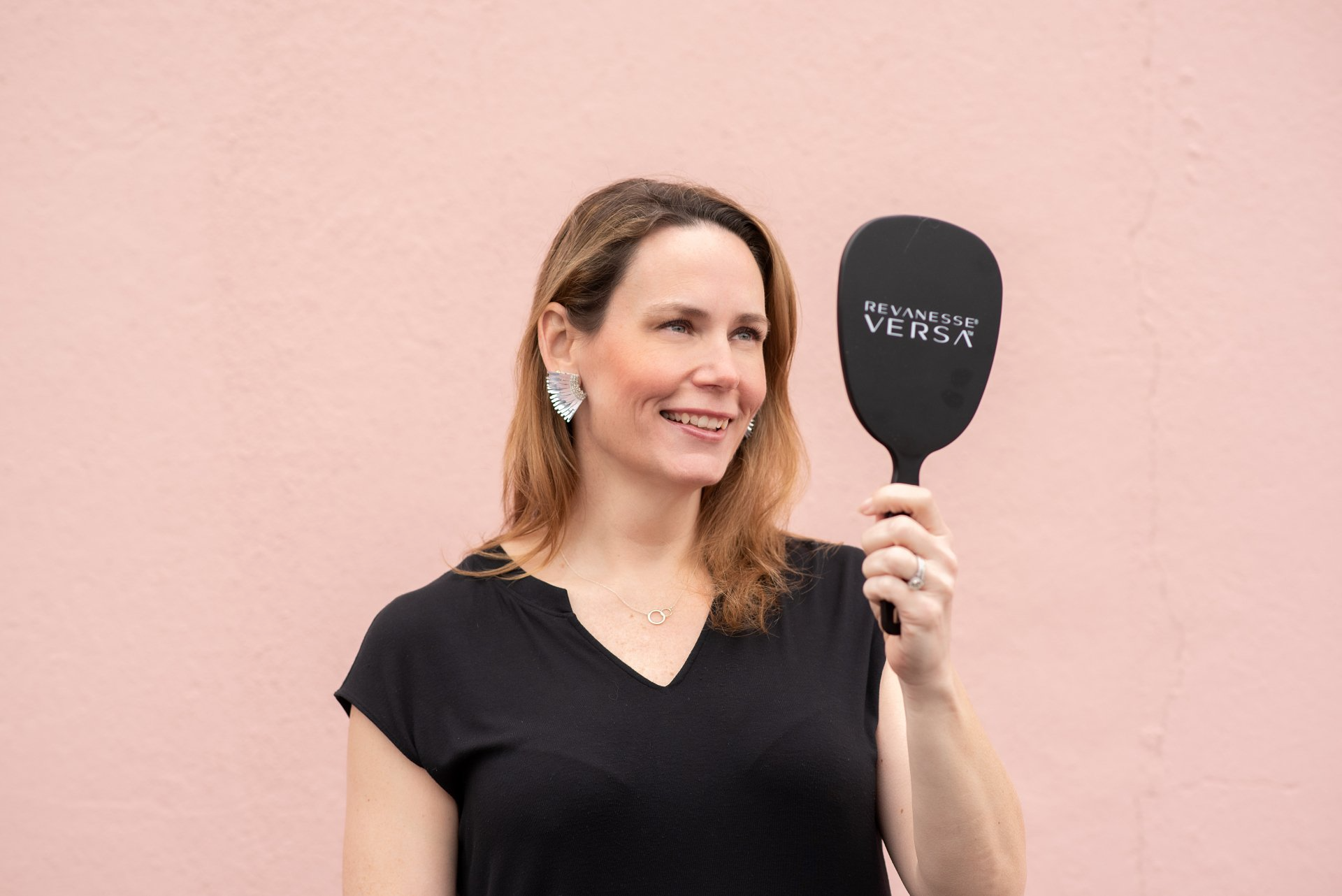 Smiling woman admiring her glowing skin in a hand mirror after receiving pre-wedding skin treatments