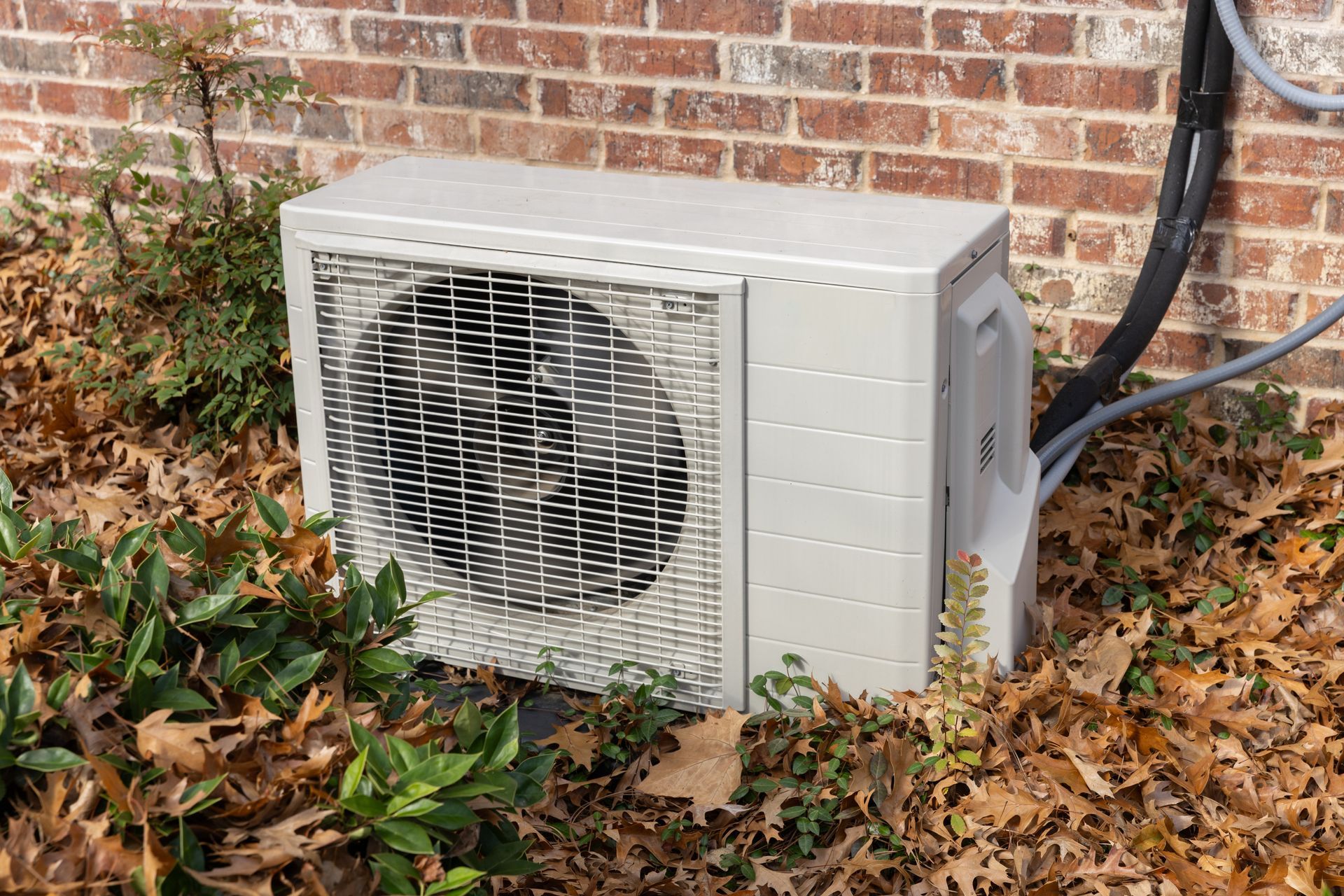 Two beige air conditioning units sit on a concrete pad next to a brick wall and a wooden fence.