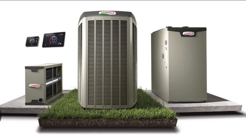 Two white HVAC outdoor condenser units sitting on a concrete pad in front of a dark, corrugated metal building.