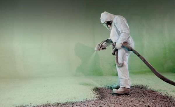 A man in a protective suit is spraying a green substance on the ground.