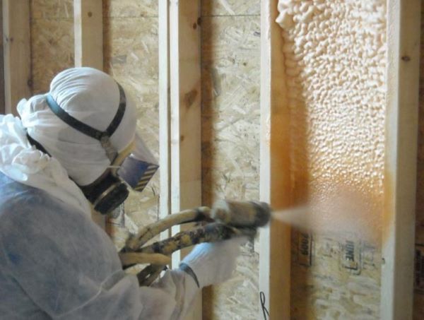 A man is spraying foam on a wooden wall.