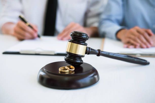 Wedding rings on a gavel while a man is signing a paper in the background, illustrating divorce law.