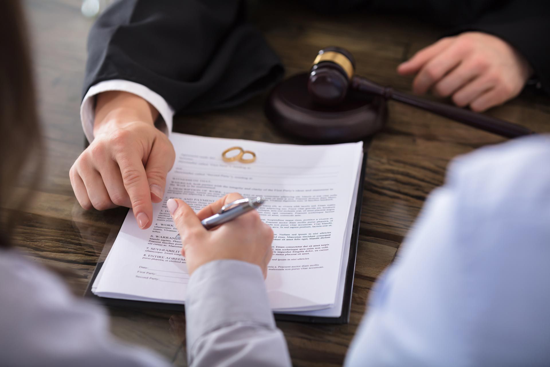 Legal document signing with rings and gavel on desk during divorce consultation meeting process review.
