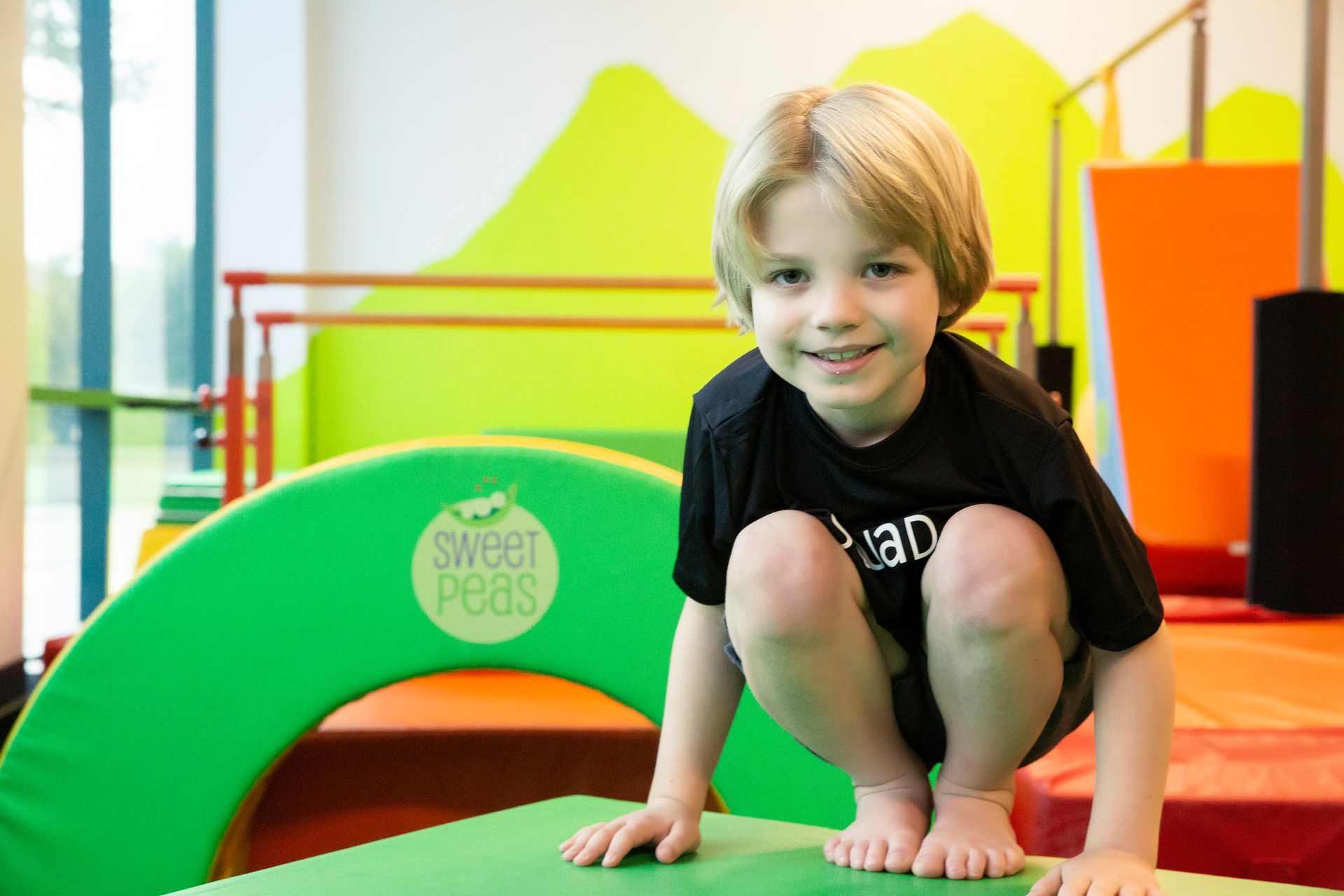 A young boy is squatting on a green mat in a gym.