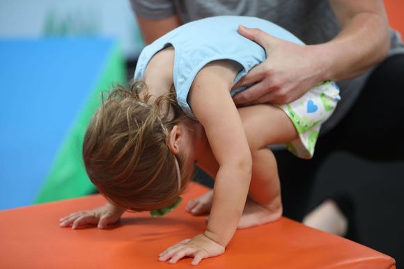 A little girl is doing a handstand on an orange mat.