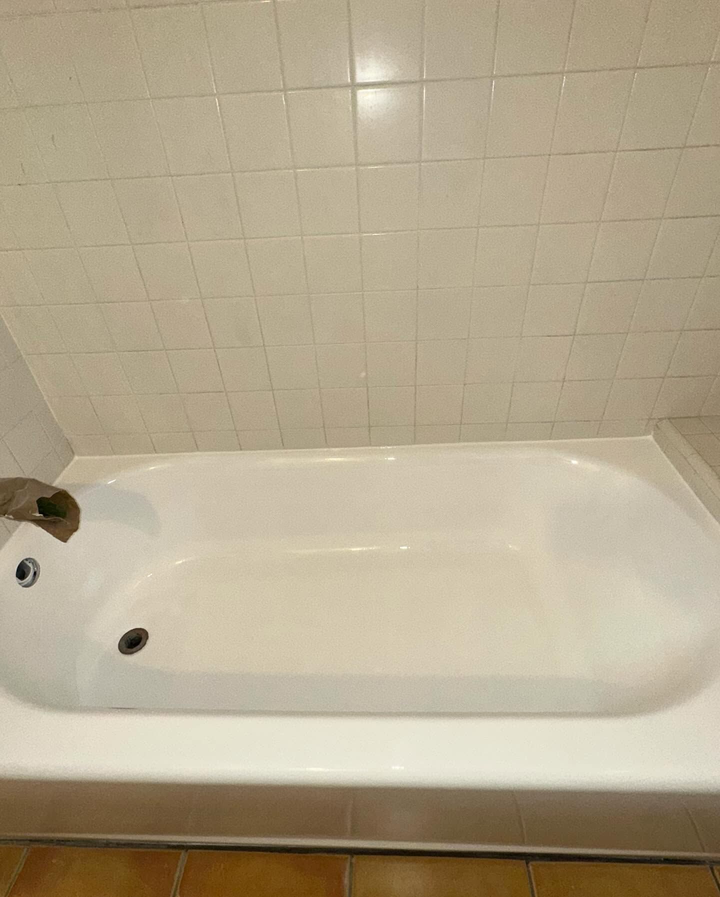 White bathtub with cream tile surround and a chrome drain stopper in a bathroom.