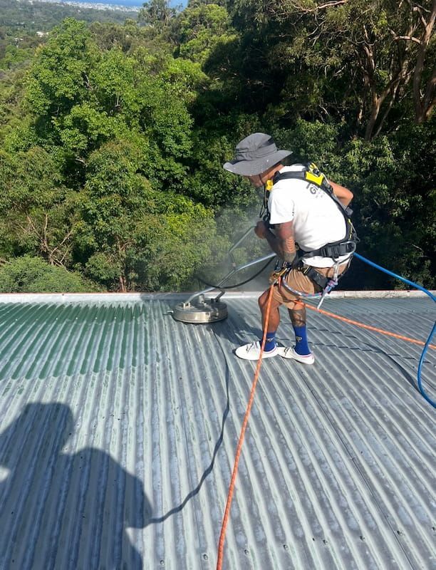 A Man is Cleaning the Roof of a Building — Dezigner Finishes Professional Painting & Decorating in Noosa Heads, QLD