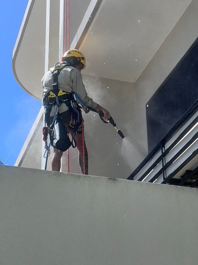 A Man is Cleaning the Side of a Building — Dezigner Finishes Professional Painting & Decorating in Noosa Heads, QLD