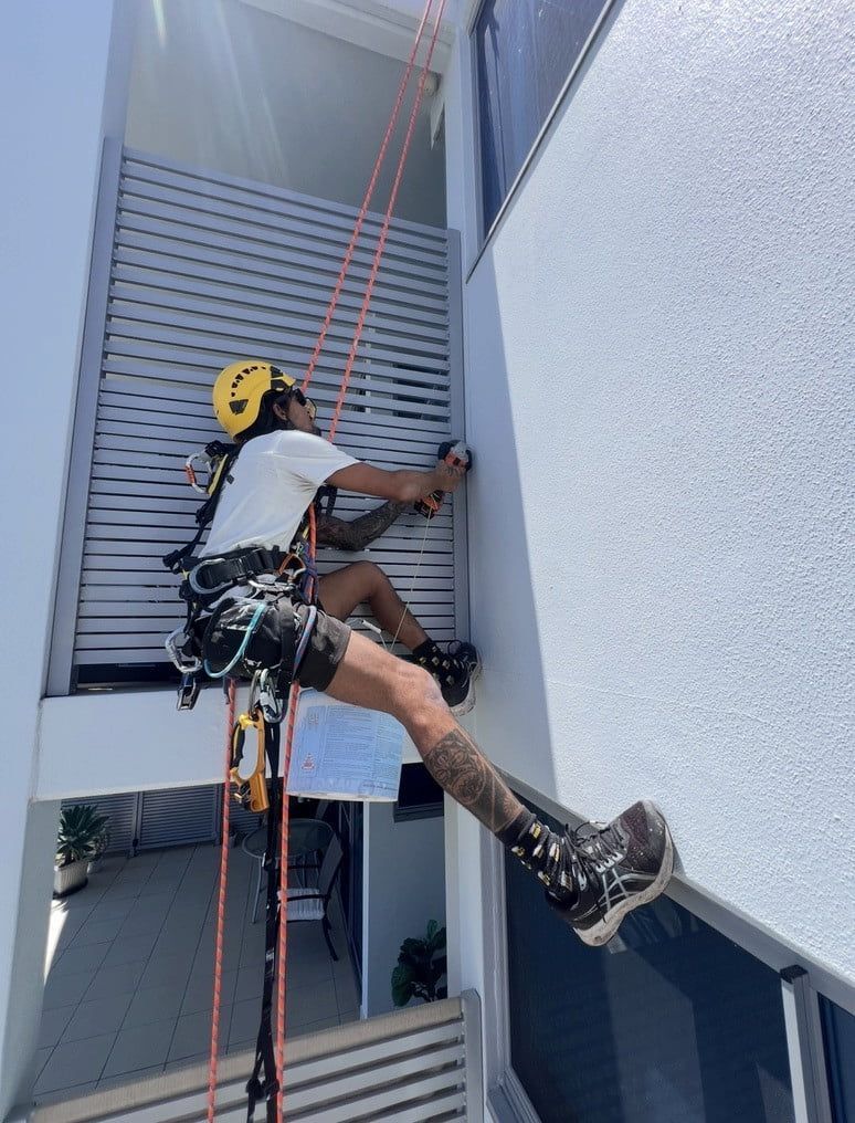 A Man is Climbing a Building With a Drill — Dezigner Finishes Professional Painting & Decorating in Sunshine Coast, QLD