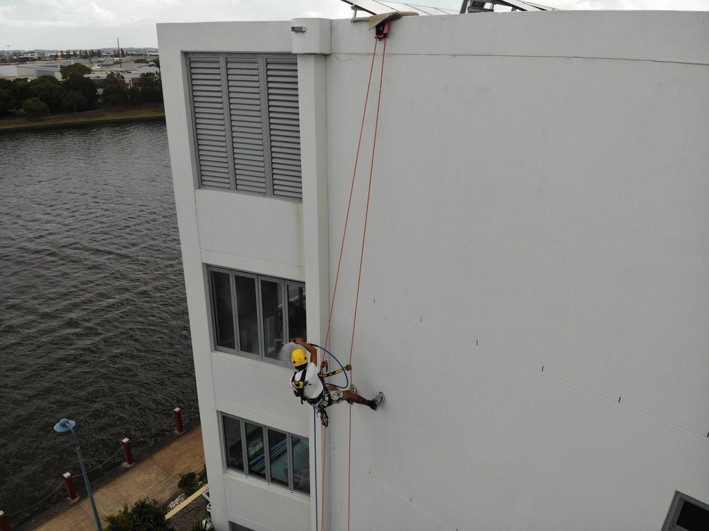 A Guy is Climbing Up the Side of a Building — Dezigner Finishes Professional Painting & Decorating in Caloundra, QLD