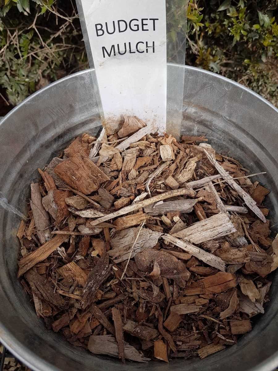 A Metal Bucket Filled With Wood Chips And A Sign That Says Budget Mulch — T&G Sand and Gravel In Sippy Downs, QLD