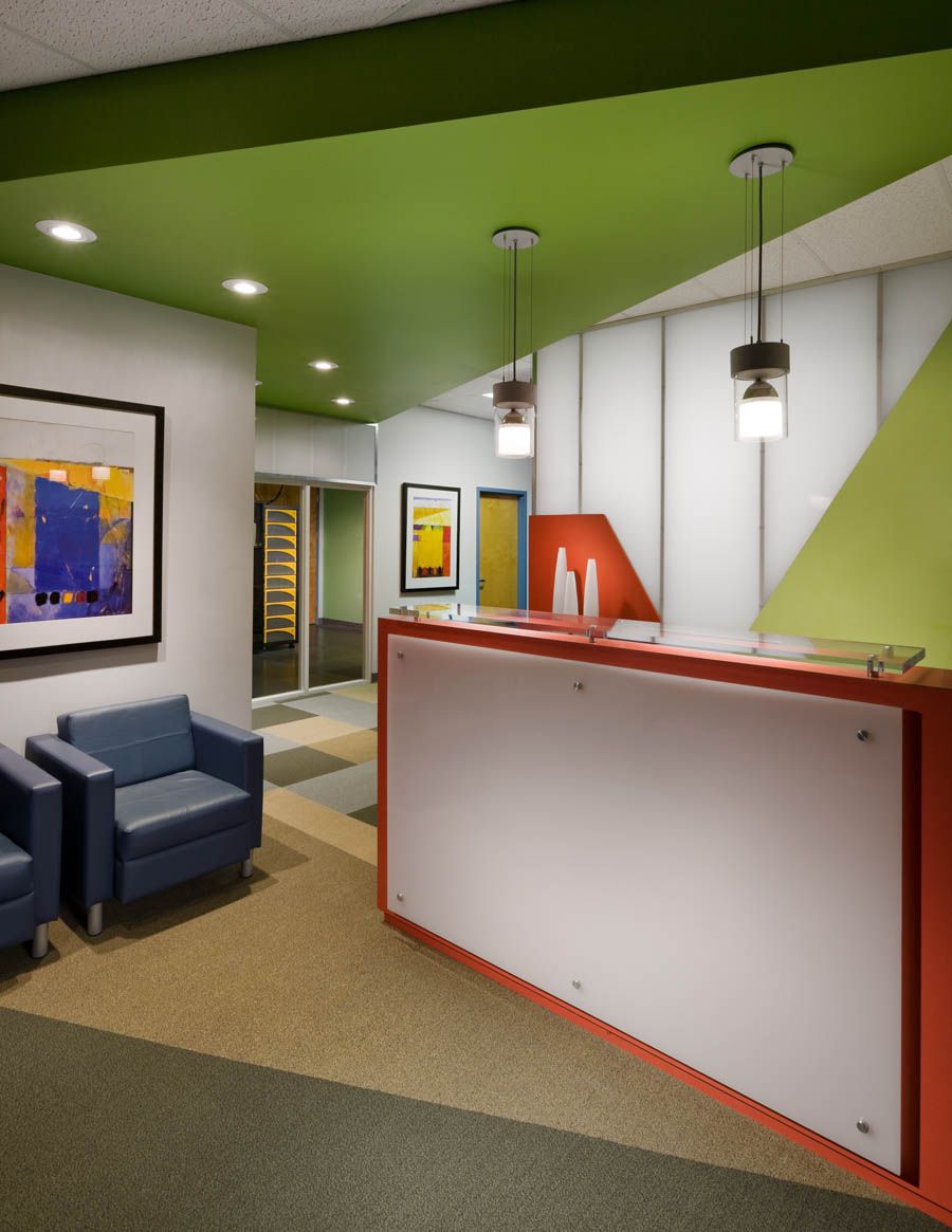 Modern office reception area with white counter, blue chairs, colorful walls, and green ceiling.